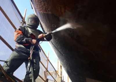 Abrasive blasting work being conducted on the hull of the the One and All Tall ship